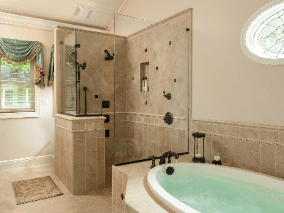 A wide shot of a luxury bathroom featuring a large, oval soaking tub filled with water in the foreground and a separate glass-walled walk-in shower with multiple showerheads and body jets in the background.