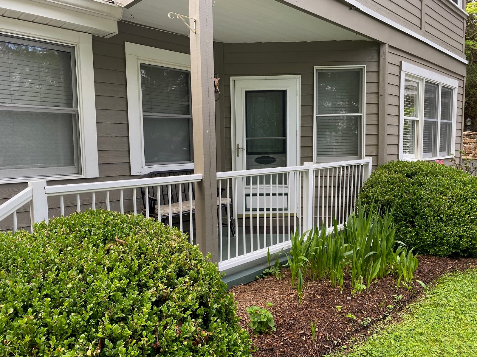 Private Entrance to the Garden Suite featuring a small porch with a white railing and a small garden with green bushes and sprouting plants in the foreground.