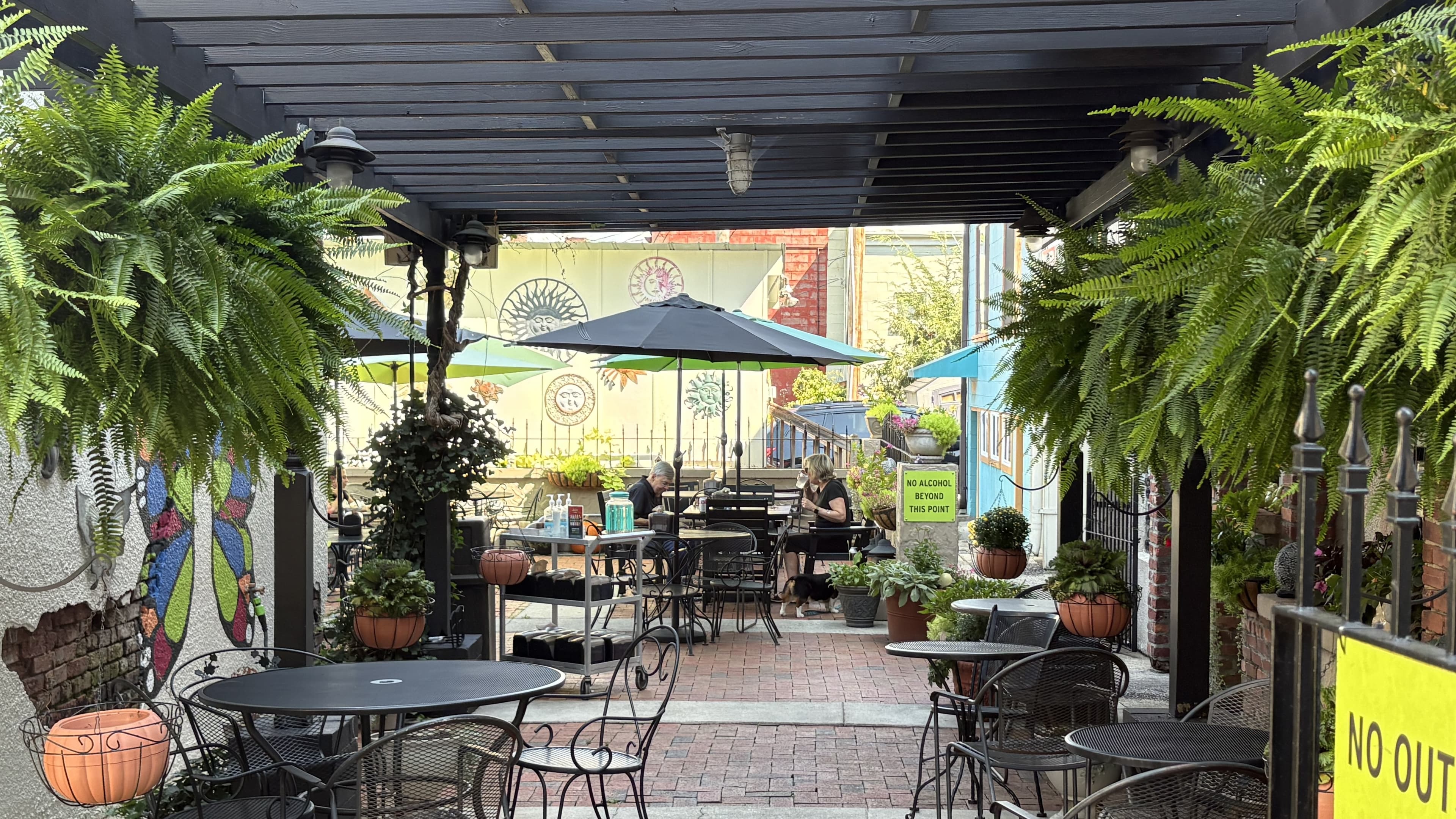 A charming outdoor dining area with greenery, bistro tables, and colorful murals.
