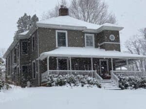 A large gray house covered in snow during a snowfall.