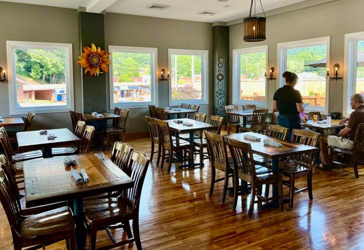 Interior of a cozy restaurant with wooden tables, a sunflower decoration, and large windows letting in natural light.