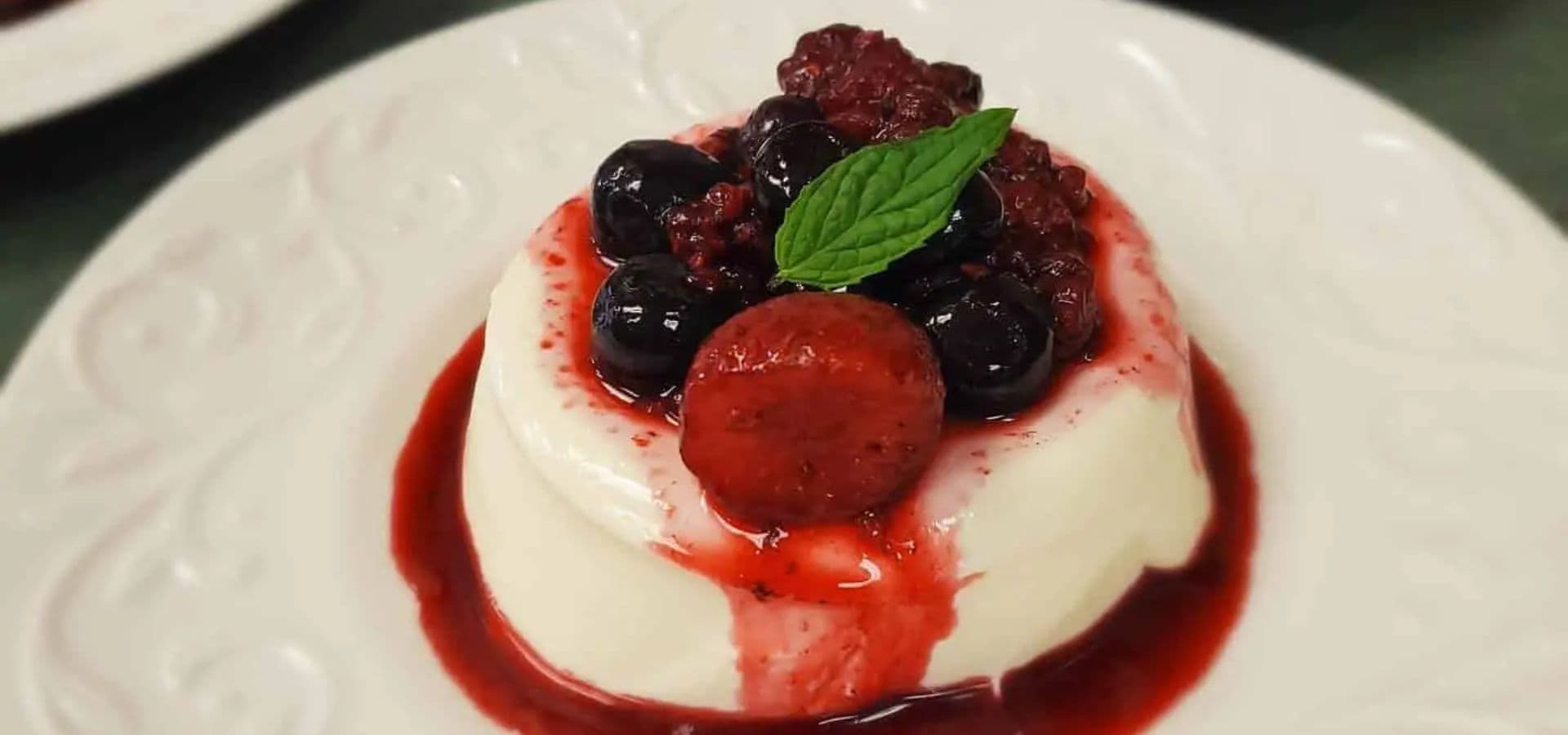 A creamy dessert topped with berries and mint on a white plate.