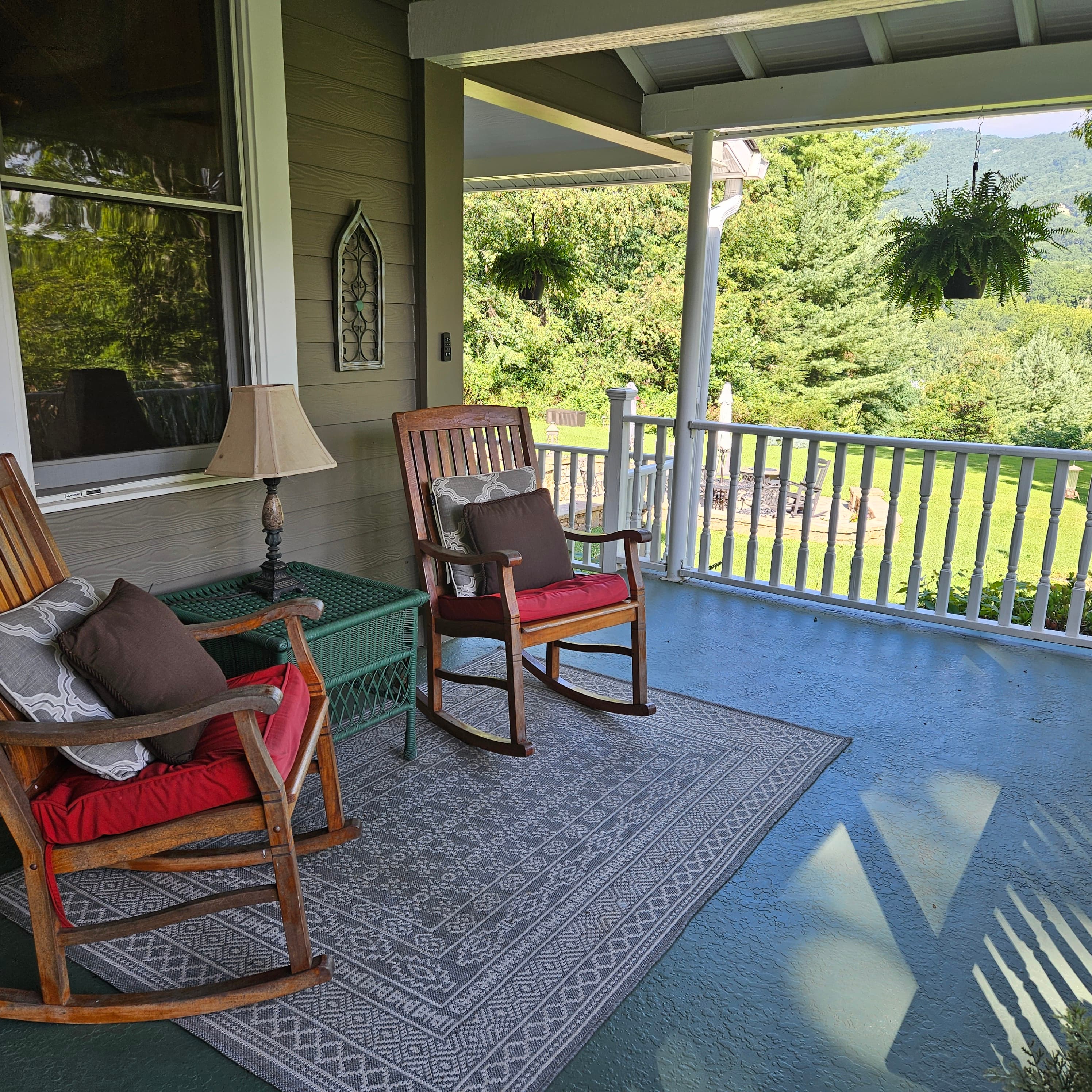 A cozy porch with two rocking chairs, a lamp, and a view of green trees.