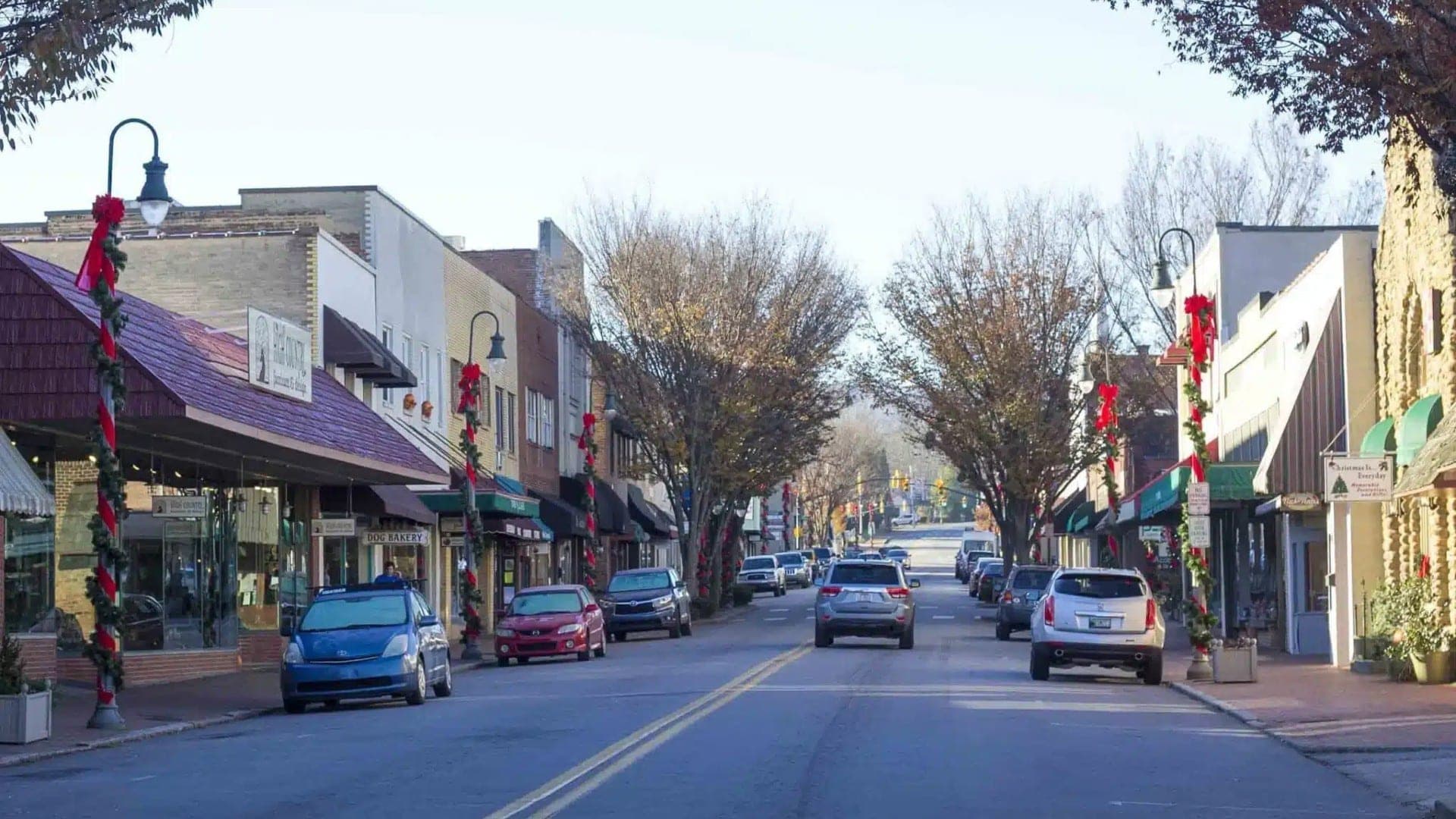 A festive downtown street lined with decorated shops and parked cars.