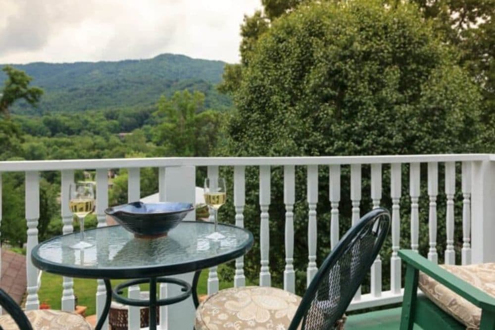A cozy balcony scene featuring a glass table with drinks and a scenic mountain view.