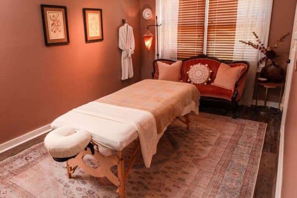 A cozy massage room featuring a treatment table, soft lighting, and decorative accents.