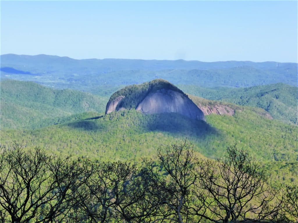 A prominent mountain peak rises above lush green hills under a clear blue sky.