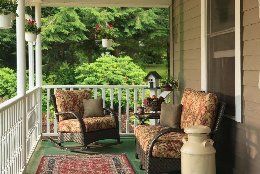 A cozy porch with floral-patterned furniture, a small table, and green surroundings.