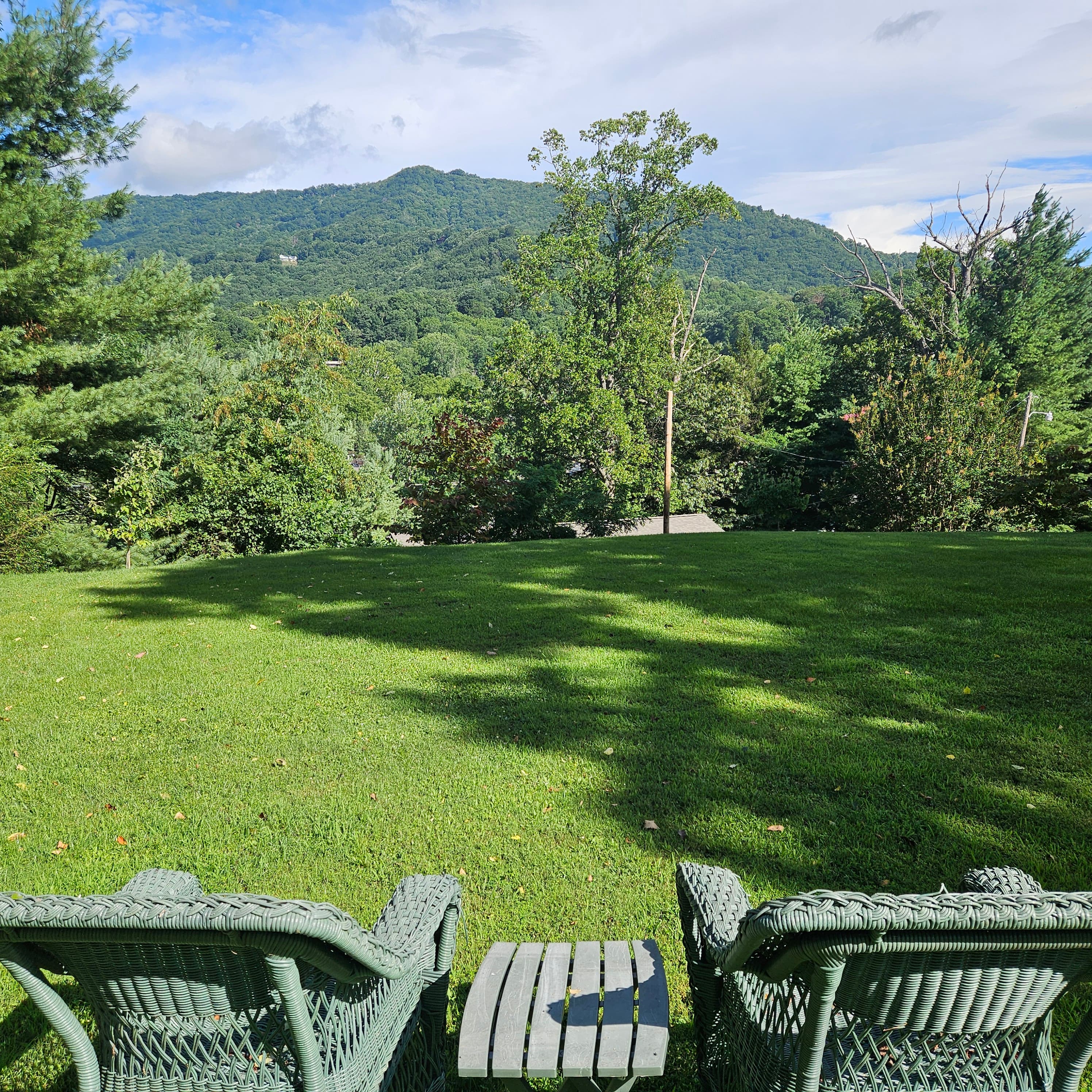 A panoramic view of a green lawn and mountains in the distance, framed by two chairs and a small table.