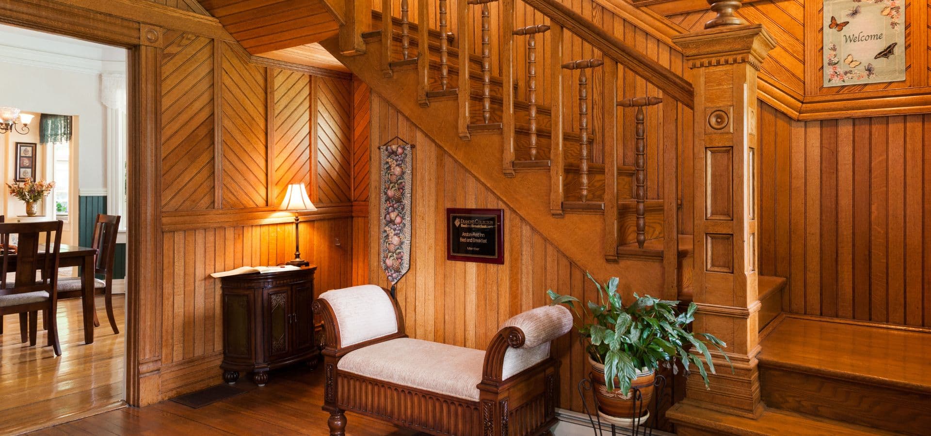A warmly lit wooden entryway featuring a staircase, a small sofa, and potted plants.