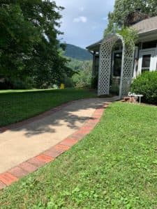 A curving concrete pathway leads to a white lattice archway in a grassy yard with mountains in the background.