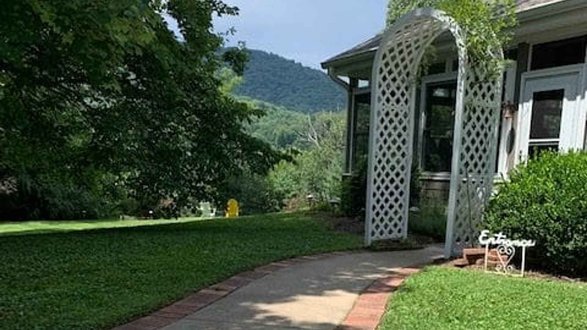 A garden path leads to a white trellis archway in a green landscape with mountains in the background. A garden path leads to a white trellis archway in a green landscape with mountains in the background.