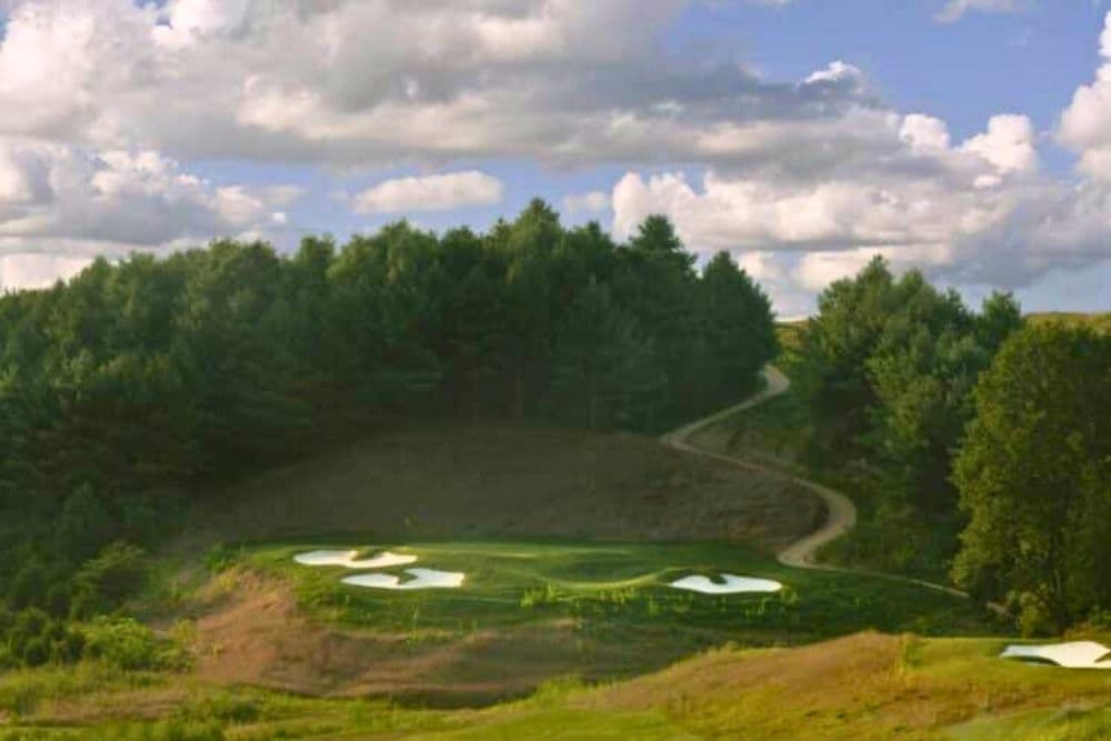 A scenic view of a golf course surrounded by trees under a cloudy sky.