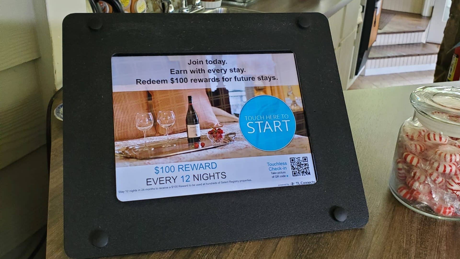 A digital kiosk promoting a rewards program for hotel stays, featuring a wine bottle and glasses on a decorative table. A digital kiosk promoting a rewards program for hotel stays, featuring a wine bottle and glasses on a decorative table.