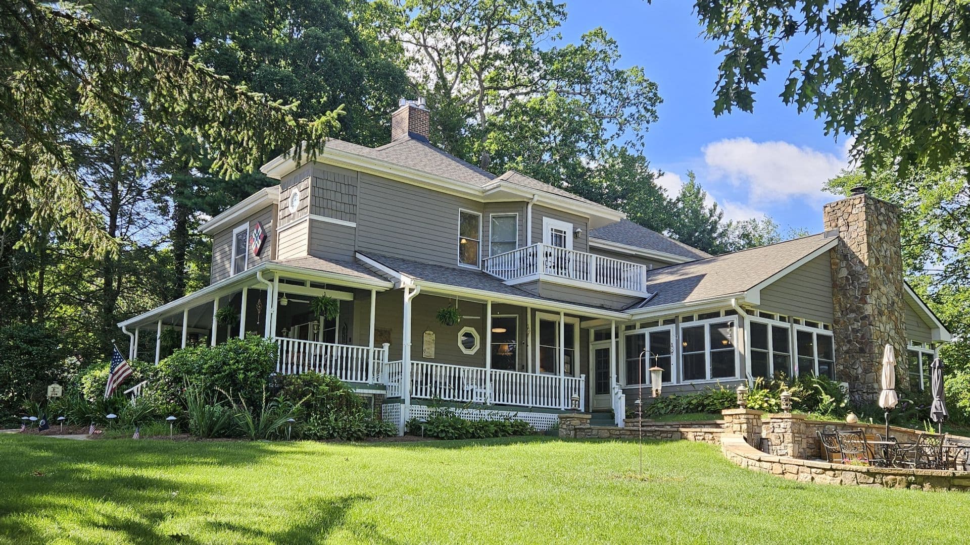 A charming two-story house with a wraparound porch, surrounded by lush greenery.