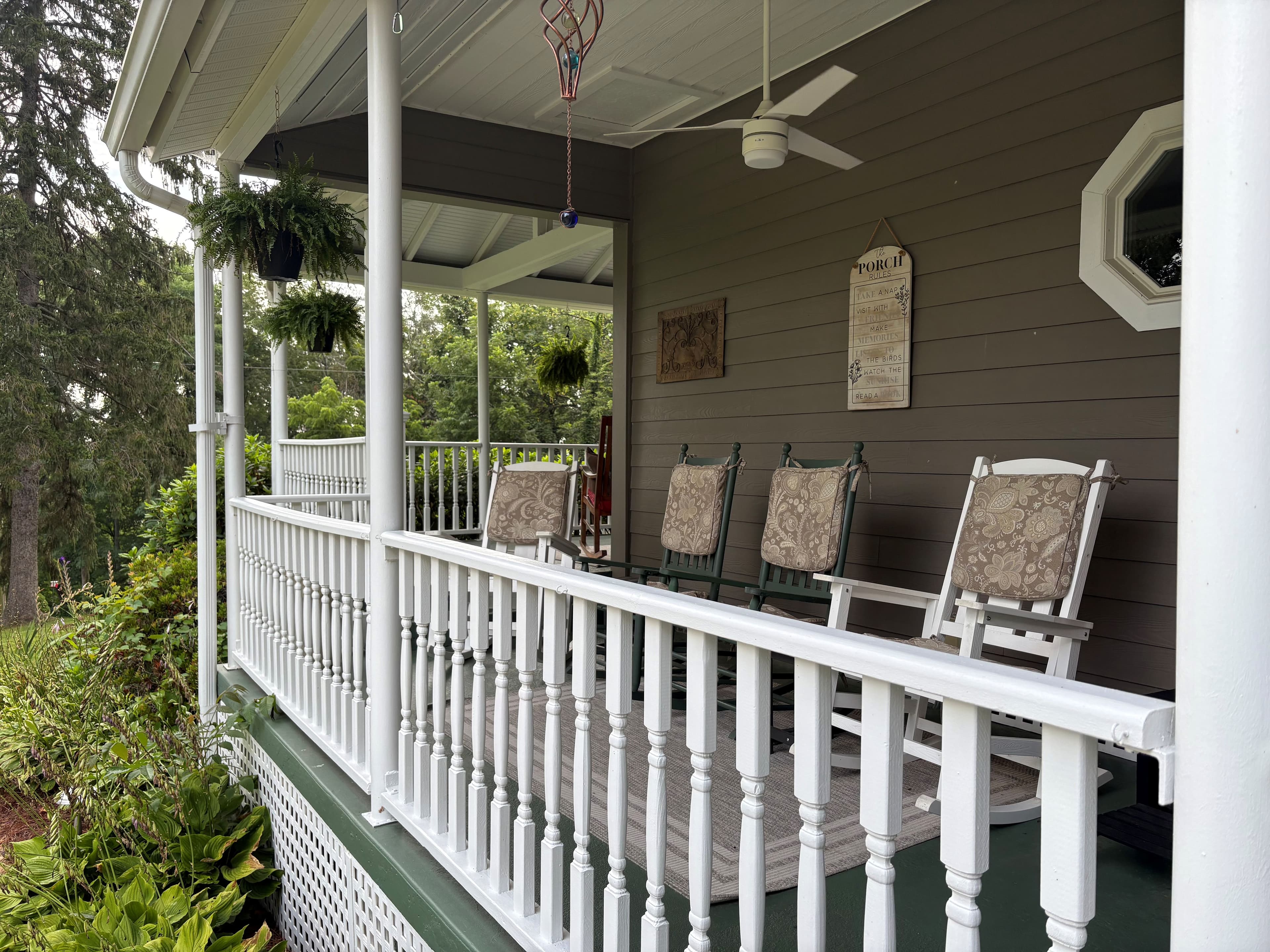 A porch with white railings, rocking chairs, and hanging plants. A porch with white railings, rocking chairs, and hanging plants.