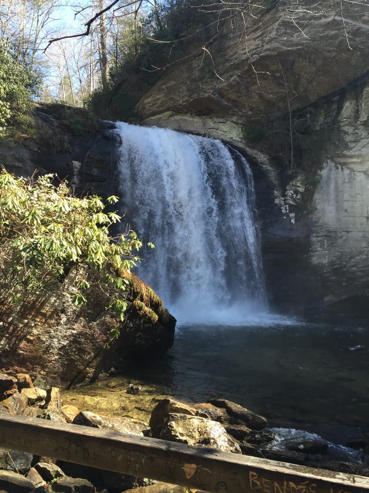 Waterfall cascading over rocks into a clear pool, surrounded by trees and greenery.