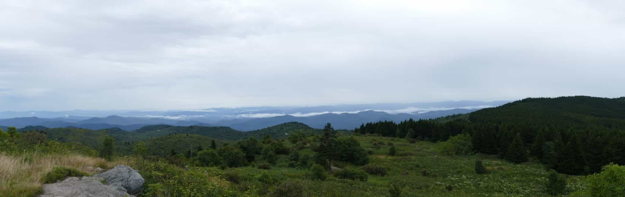 A panoramic view of rolling green hills and distant mountains under a cloudy sky.