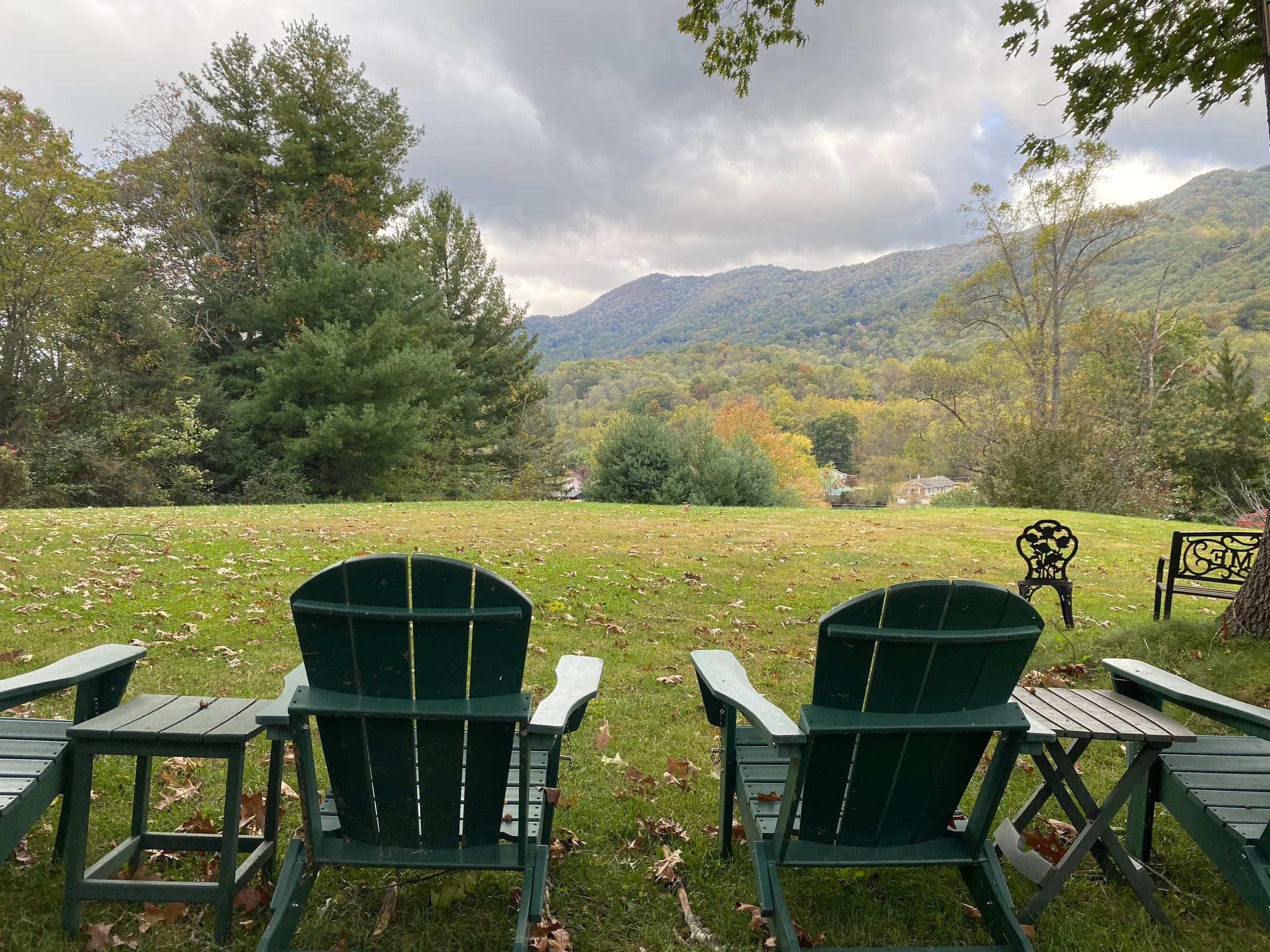 Two green Adirondack chairs overlook a valley with rolling hills and trees under a cloudy sky. Two green Adirondack chairs overlook a valley with rolling hills and trees under a cloudy sky.