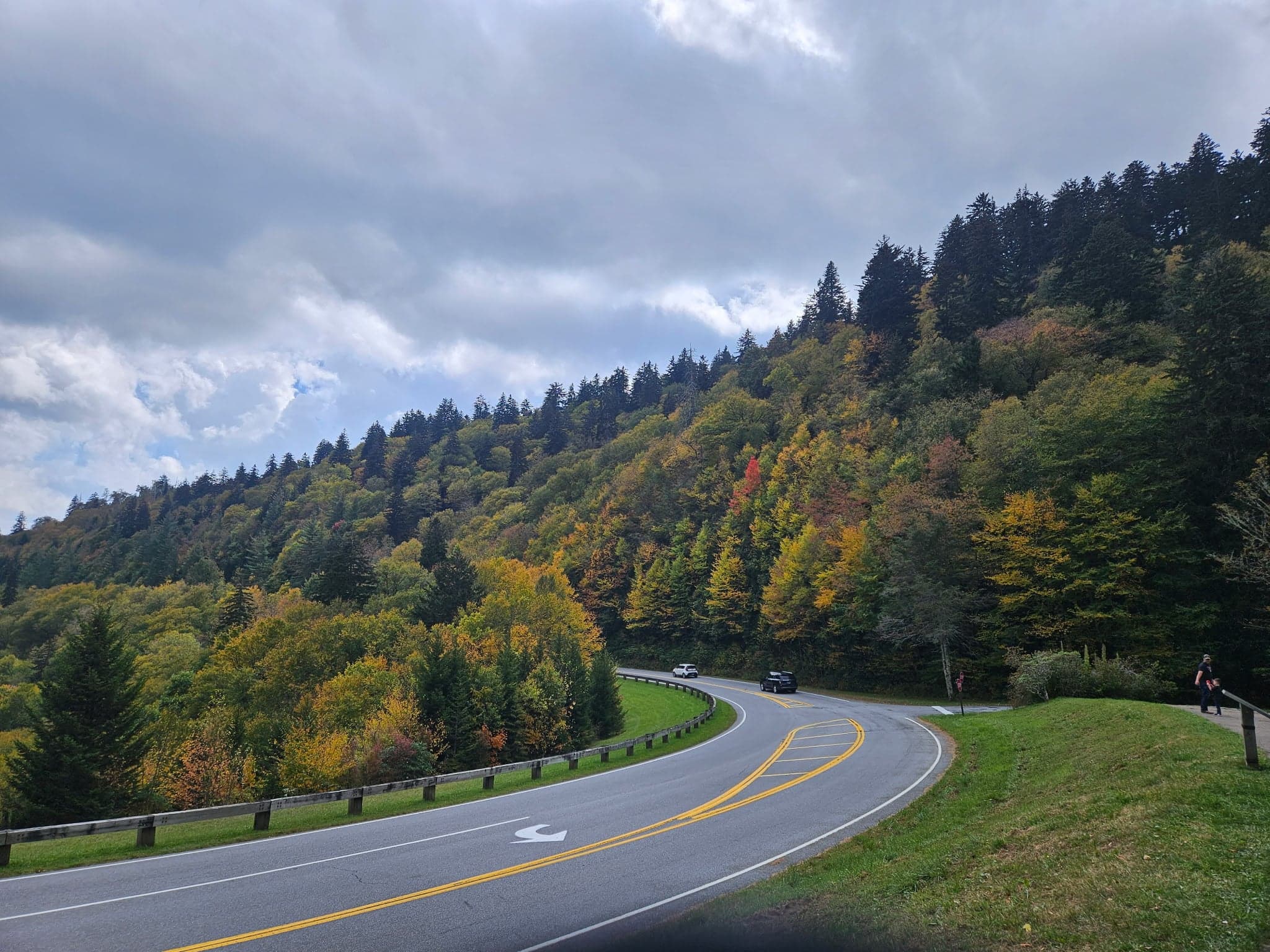A winding road curves through a forested landscape with colorful autumn foliage under a cloudy sky. A winding road curves through a forested landscape with colorful autumn foliage under a cloudy sky.
