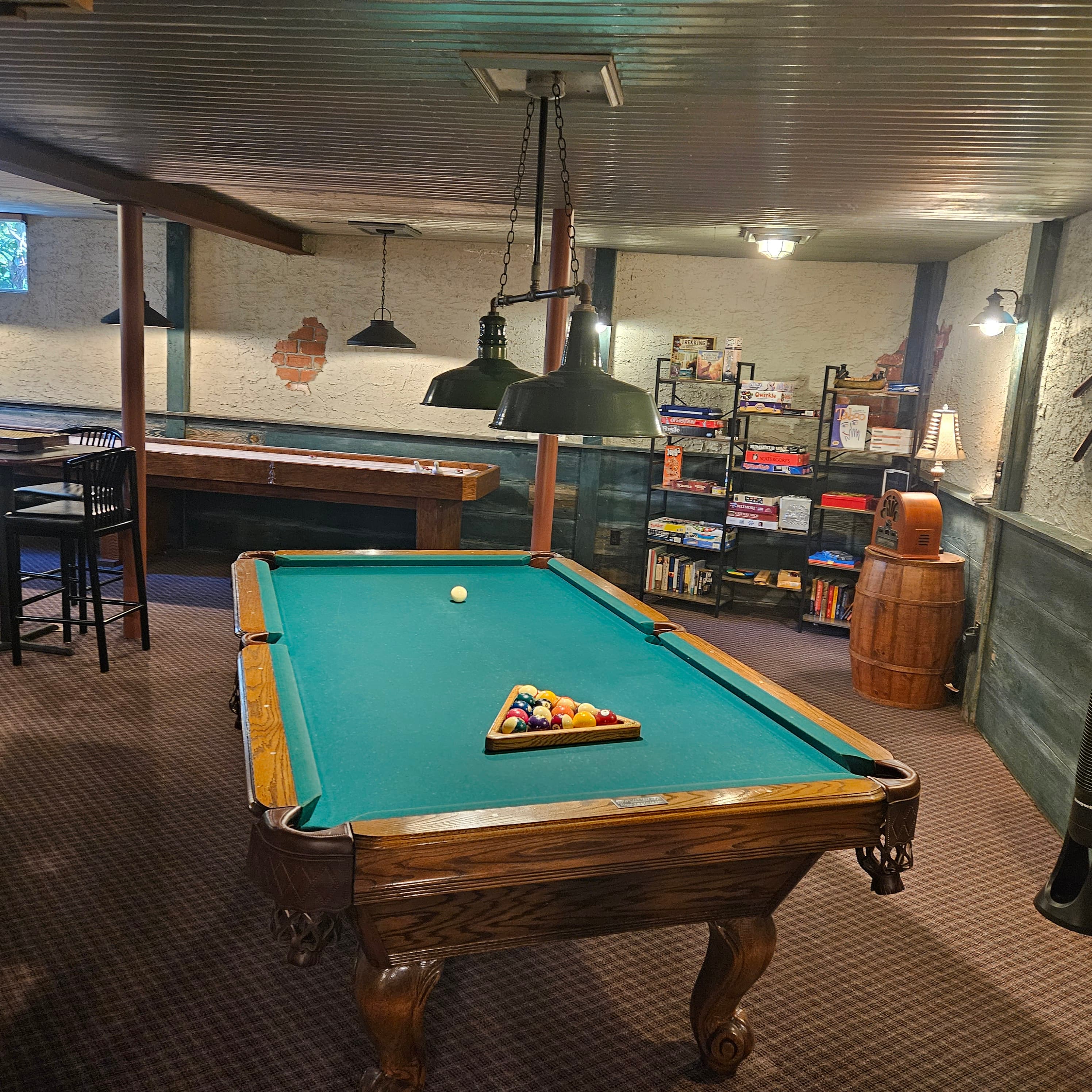A cozy basement game room featuring a pool table, bar stools, and shelves of books.