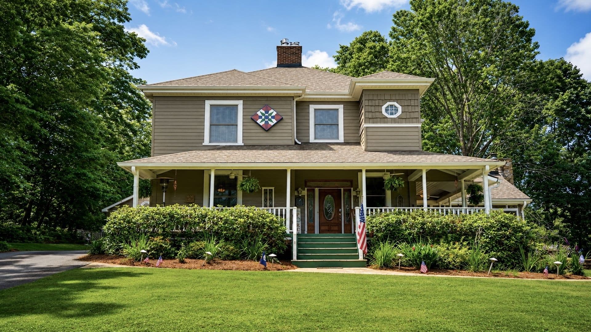 A two-story house with a porch, greenery, and a decorative quilt block on the facade.