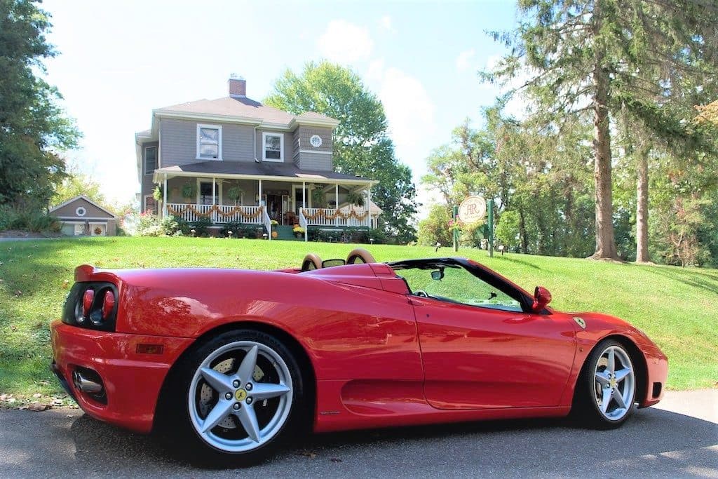 A red convertible sports car parked in front of a two-story house surrounded by trees.