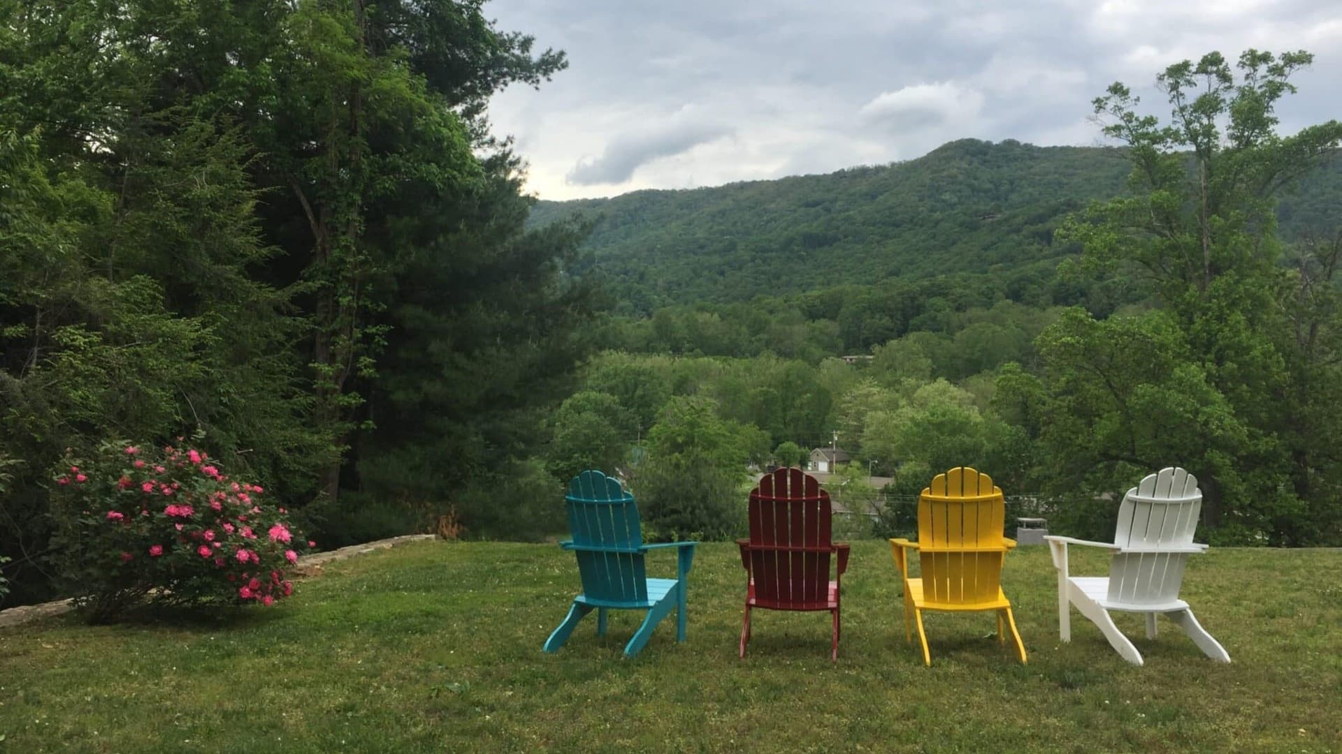 Four colorful Adirondack chairs facing a scenic mountain view surrounded by greenery. Four colorful Adirondack chairs facing a scenic mountain view surrounded by greenery.