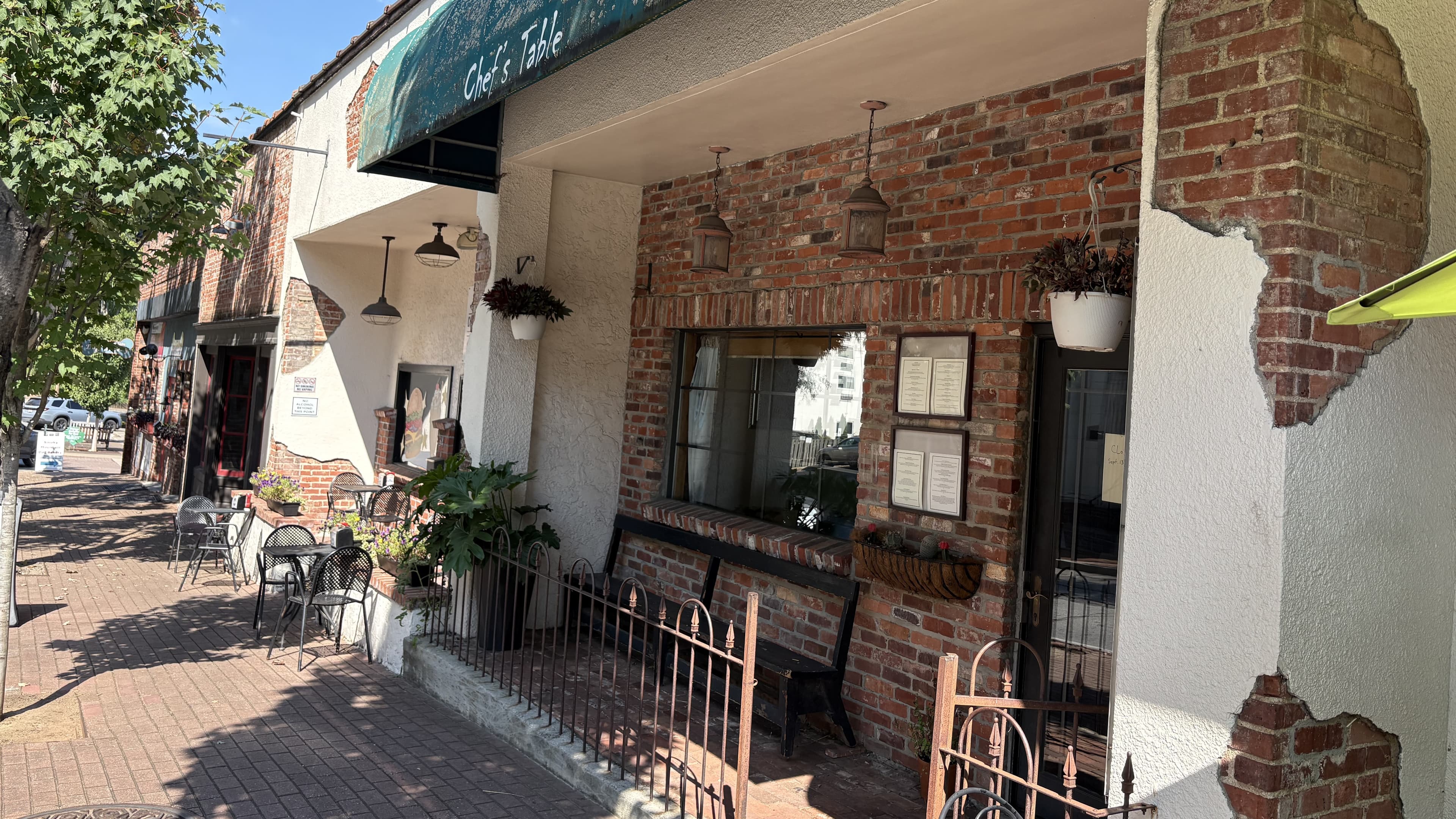 A brick restaurant exterior with outdoor seating and hanging plants.