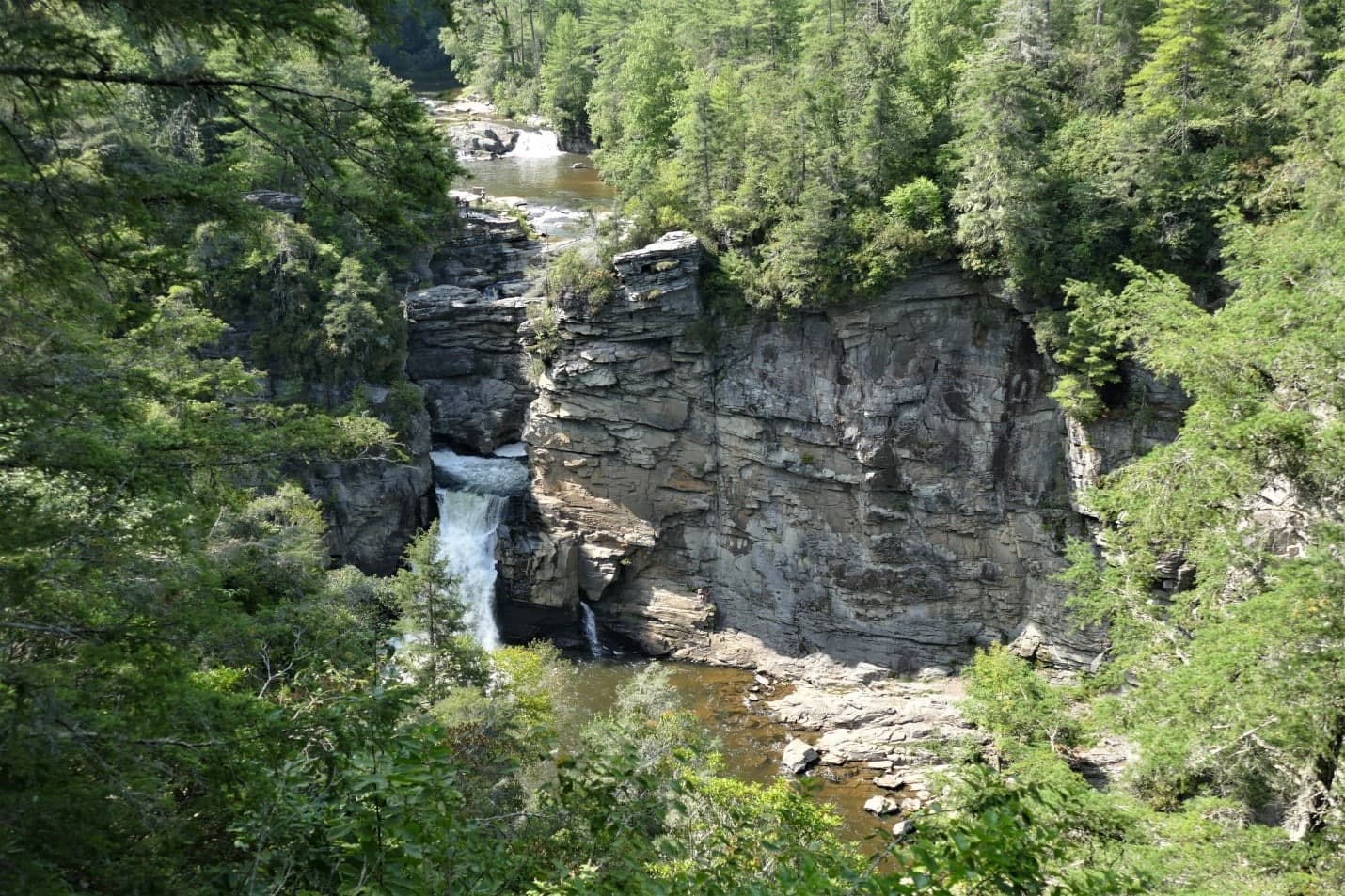 A waterfall cascades over rocky cliffs surrounded by lush greenery.