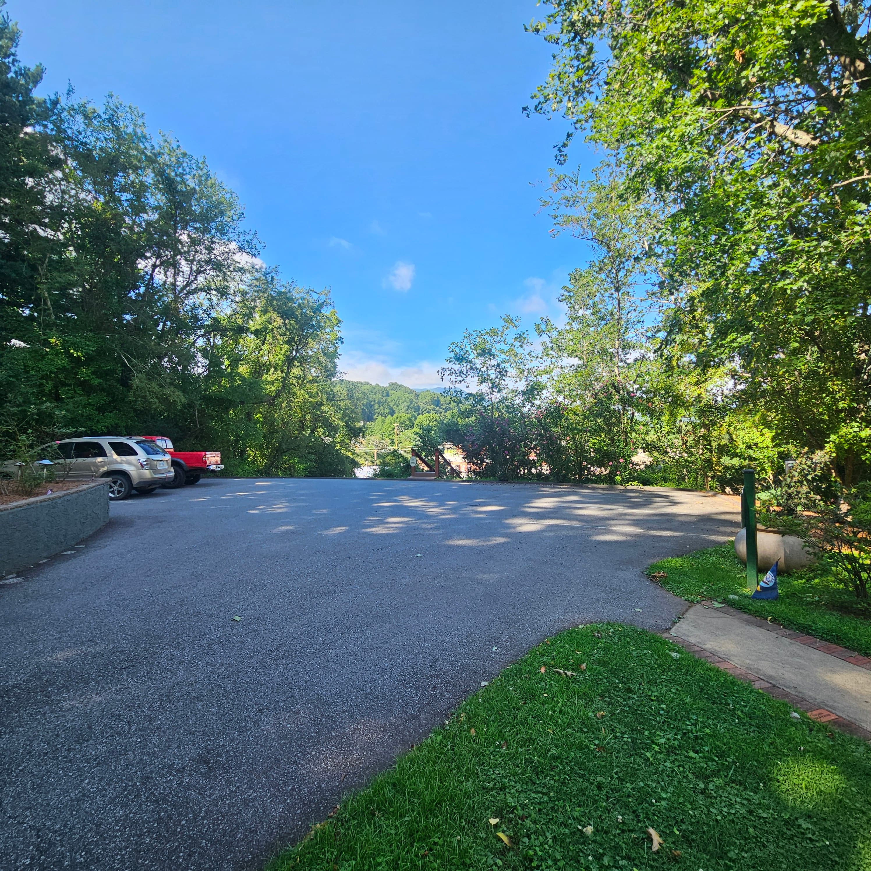 A clear, empty parking area surrounded by trees and a blue sky.