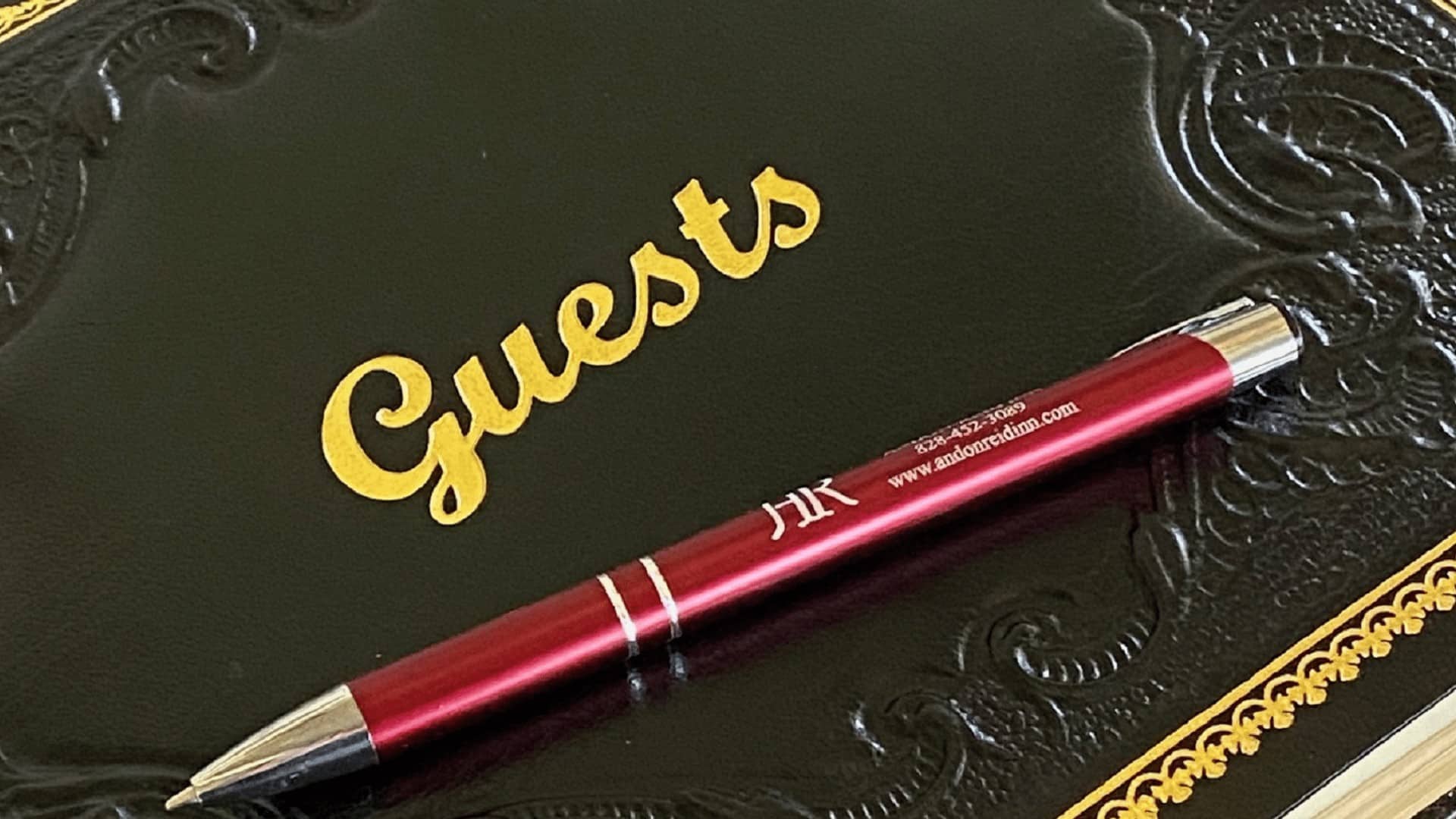 A red pen lies on a black guestbook embossed with the word "Guests" in gold. A red pen lies on a black guestbook embossed with the word "Guests" in gold.