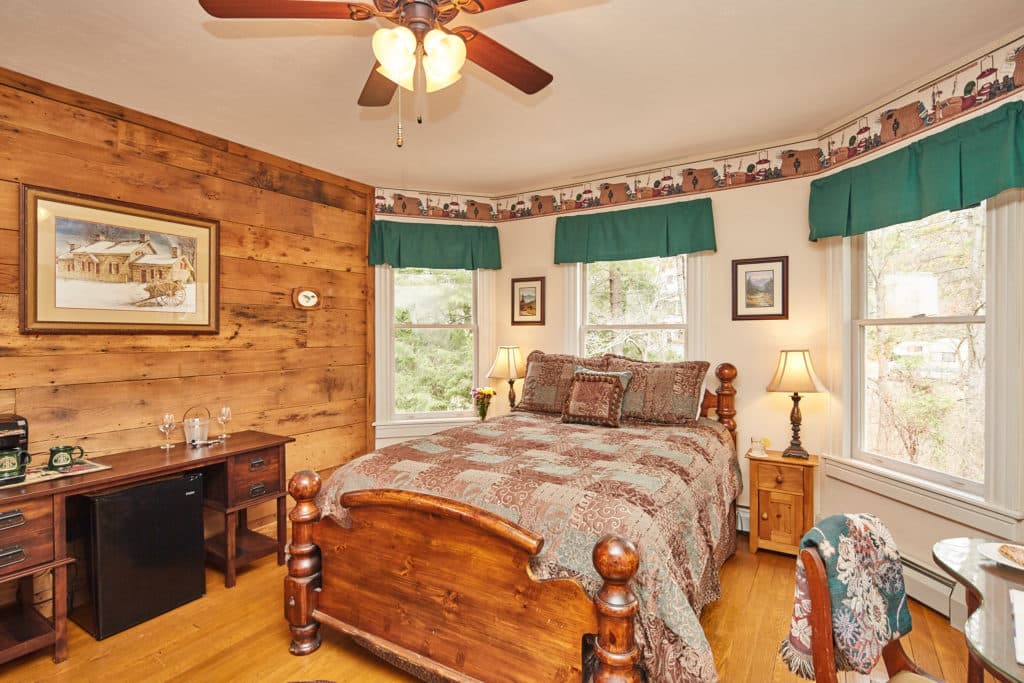 A cozy bedroom featuring a wooden bed, desk, and large windows with green drapes.