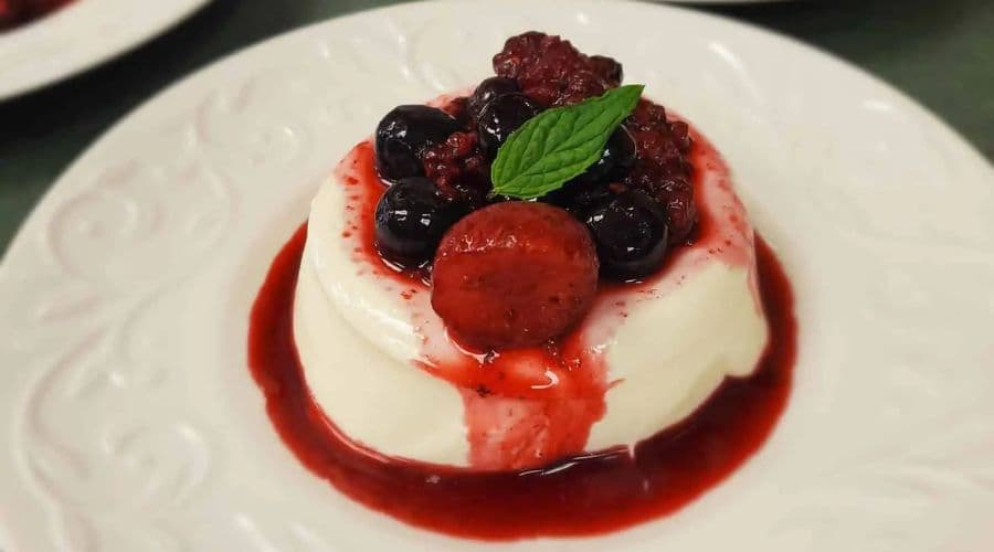 A creamy panna cotta topped with mixed berries and a mint leaf.