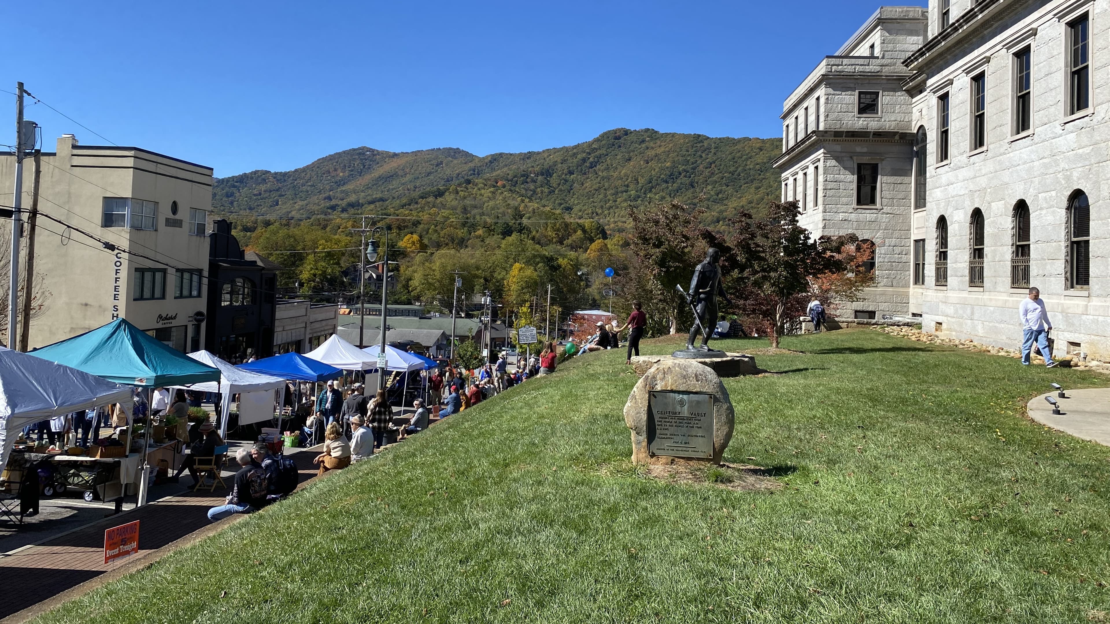 A bustling outdoor market with tents and people set against a backdrop of mountains and a historic building.