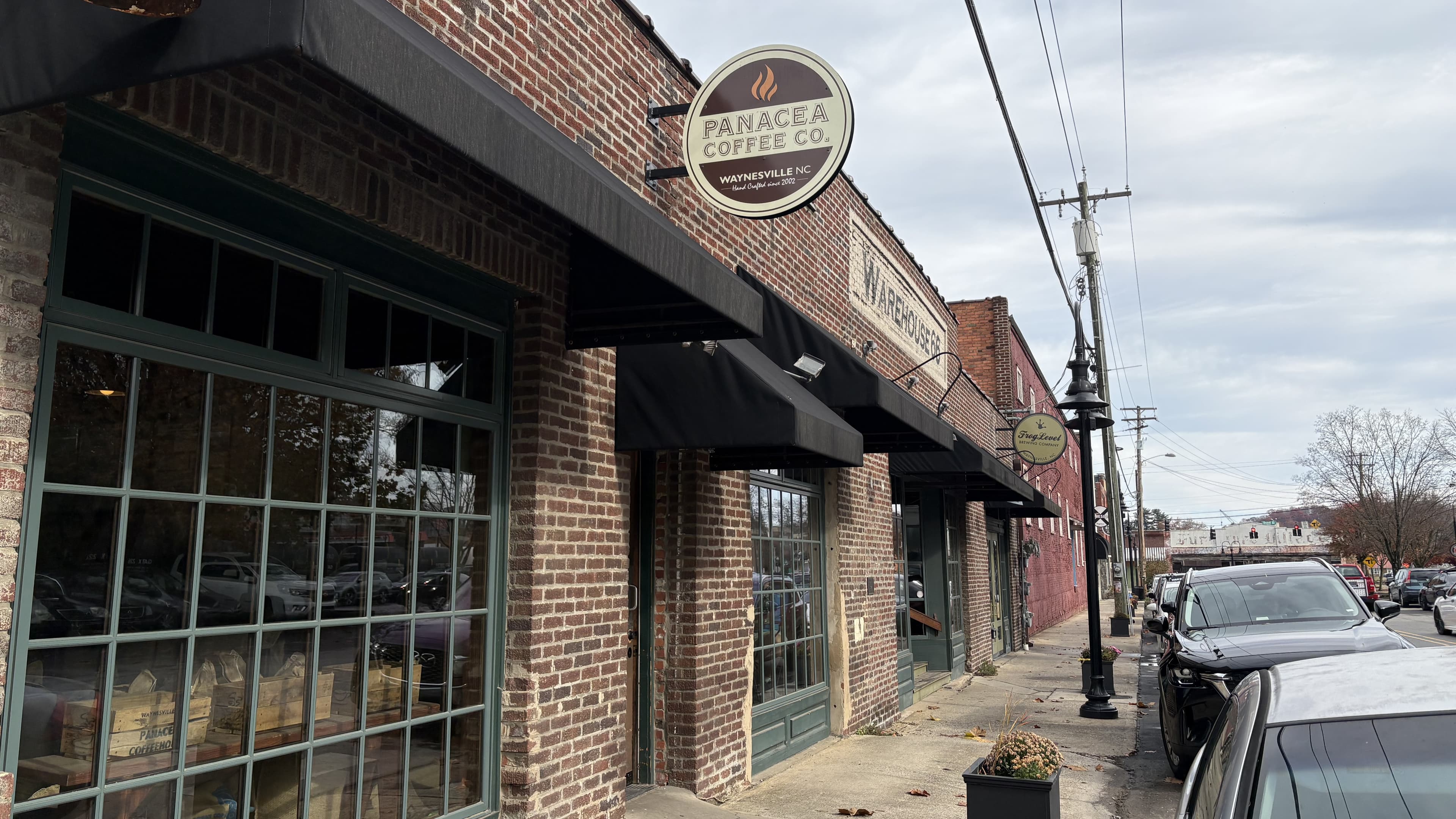 Exterior of Panacea Coffee Co. featuring brick facade and storefronts on a cloudy day.