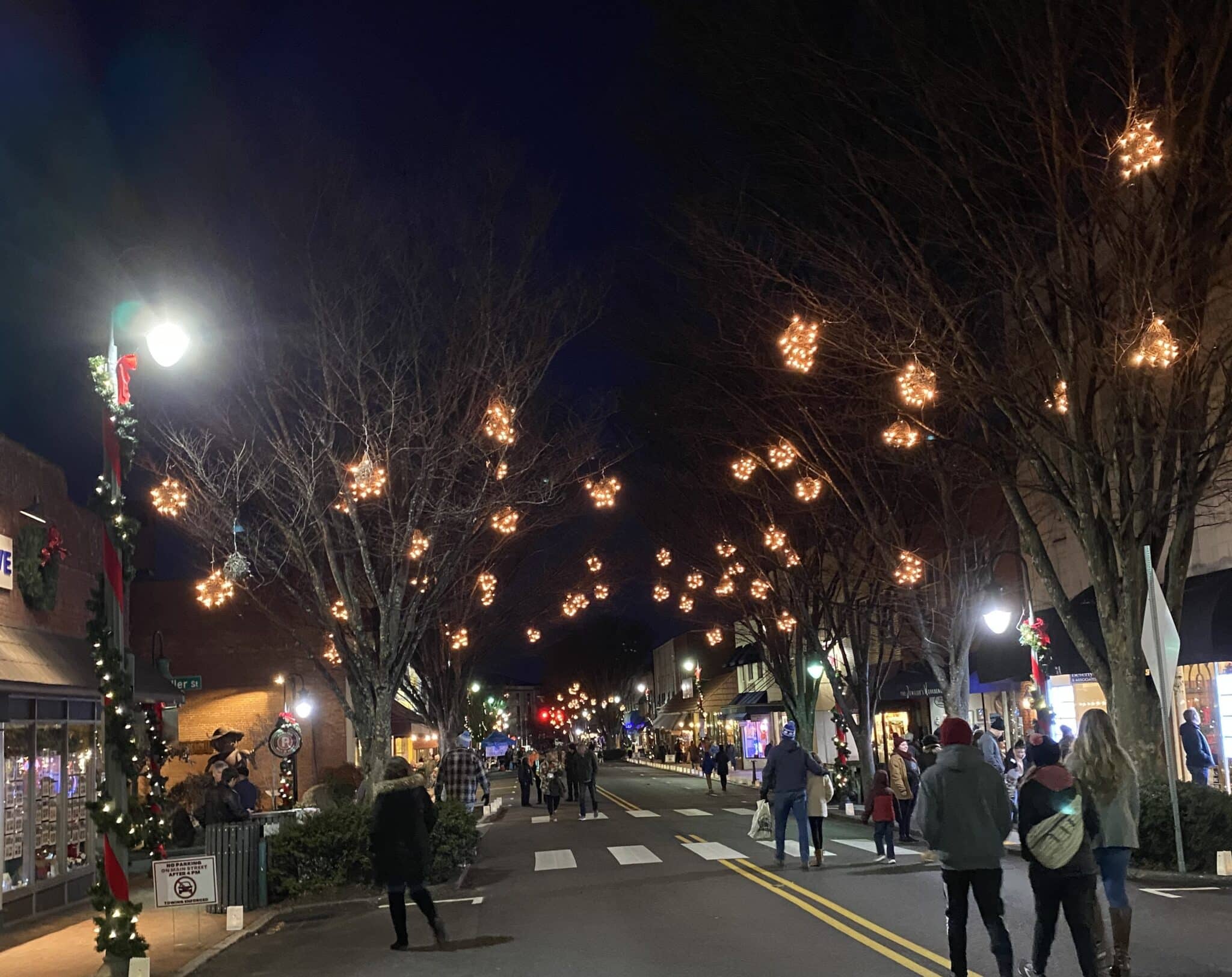 A festive street at night lined with trees decorated with star-shaped lights, bustling with people. A festive street at night lined with trees decorated with star-shaped lights, bustling with people.