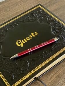 A black guestbook with gold lettering and a red pen placed on top.
