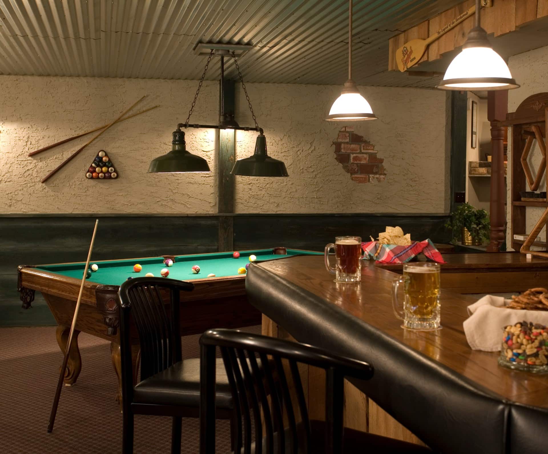 A cozy game room featuring a pool table, two beers on the bar, and snacks. A cozy game room featuring a pool table, two beers on the bar, and snacks.