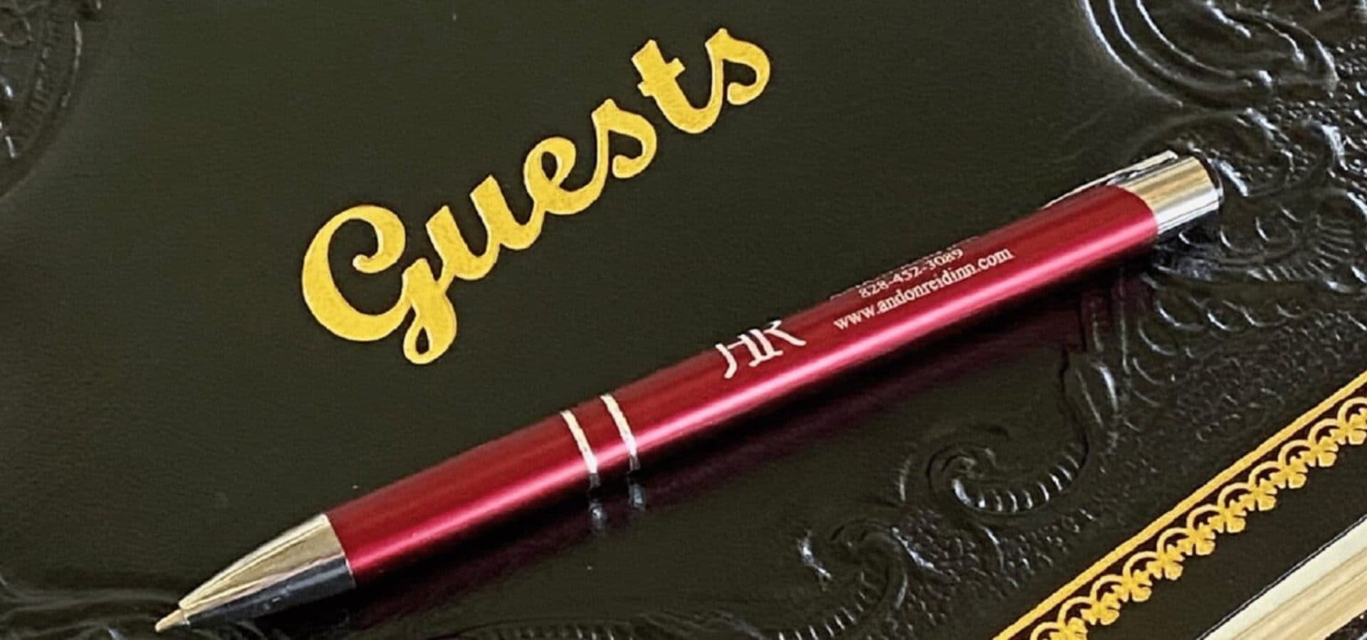 A red pen rests on a black guestbook embossed with "Guests" in gold lettering.