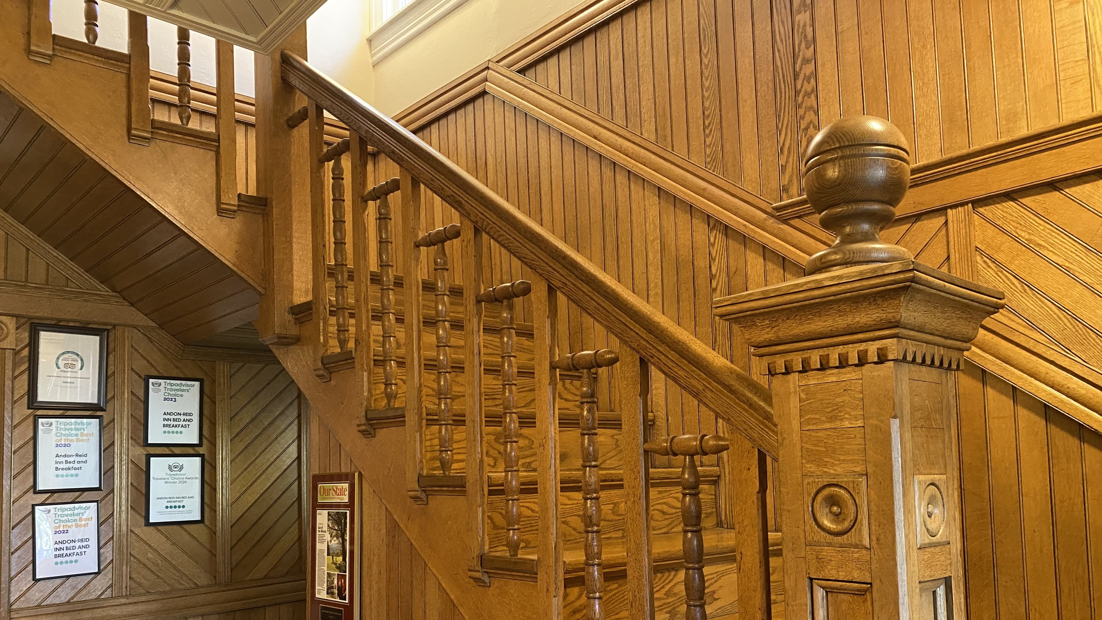 A wooden staircase with decorative railings and a wall featuring framed papers.
