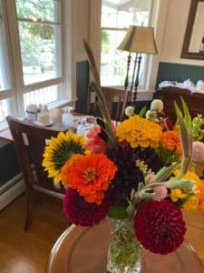 A vibrant bouquet of mixed flowers in a glass vase on a wooden table, with a cozy room in the background.
