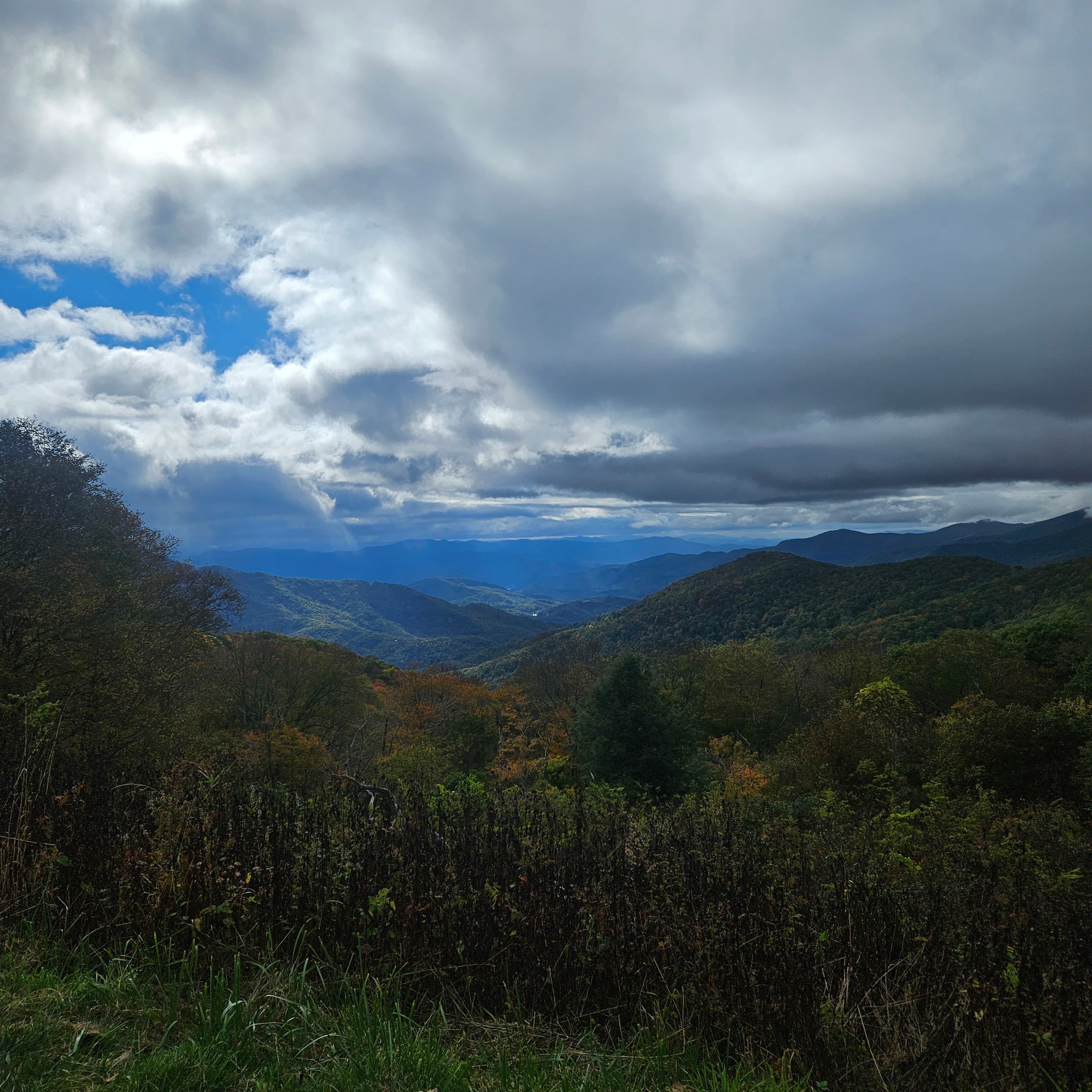 A scenic landscape featuring rolling mountains under a cloudy sky, with patches of blue peeking through. A scenic landscape featuring rolling mountains under a cloudy sky, with patches of blue peeking through.