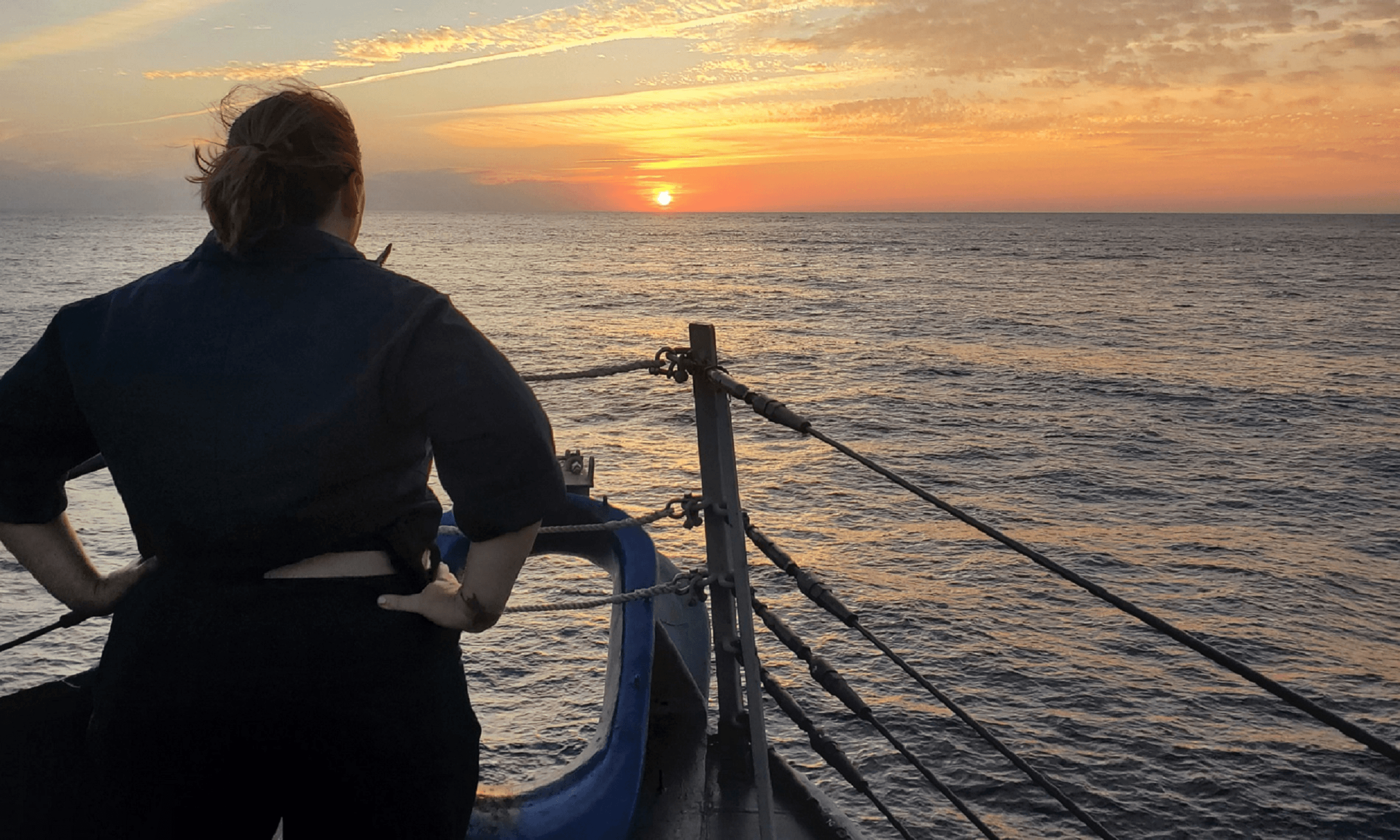 A person stands on a boat, watching a vibrant sunset over the ocean. A person stands on a boat, watching a vibrant sunset over the ocean.