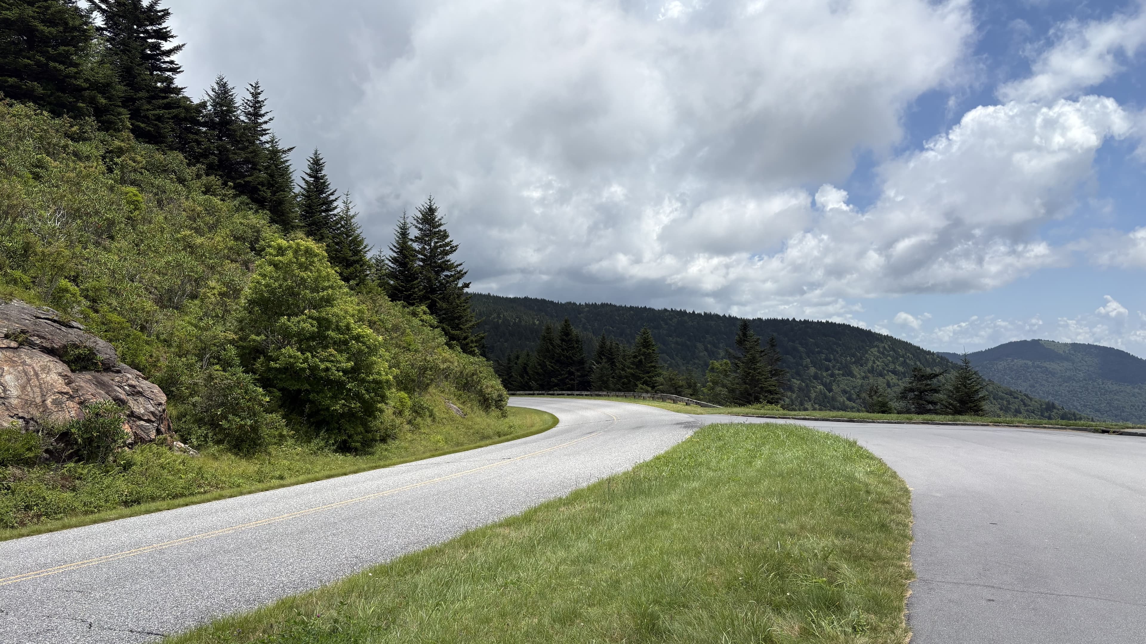 Winding road curves through green hills under a partly cloudy sky.