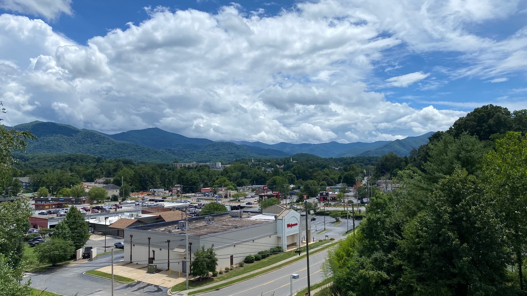 A scenic view of a town surrounded by mountains under a partly cloudy sky.
