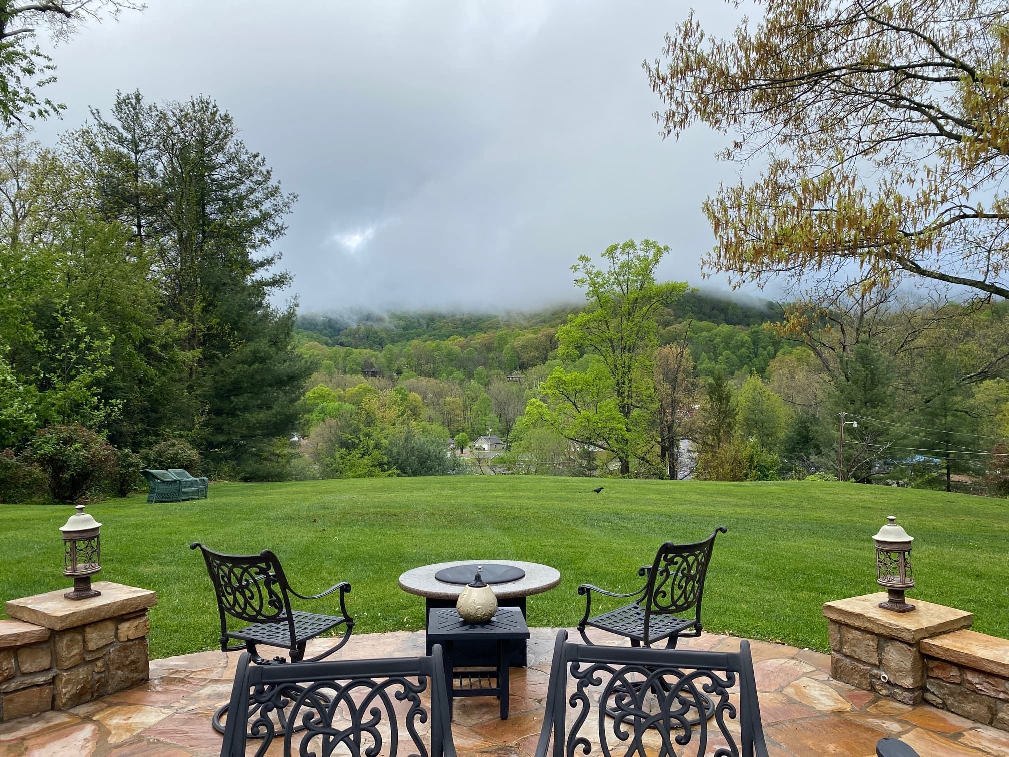 A picturesque backyard view featuring a stone patio, seating area, and lush greenery under a cloudy sky. A picturesque backyard view featuring a stone patio, seating area, and lush greenery under a cloudy sky.