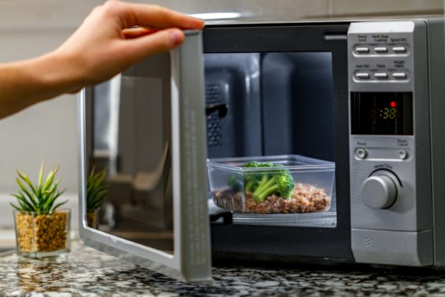 hand opening microwave containng broccoli and rice