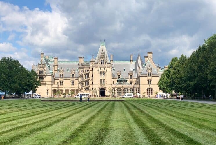 Exterior view of the front of an expansive castle-like estate surrounded by pristinely cut grass and blue skies above