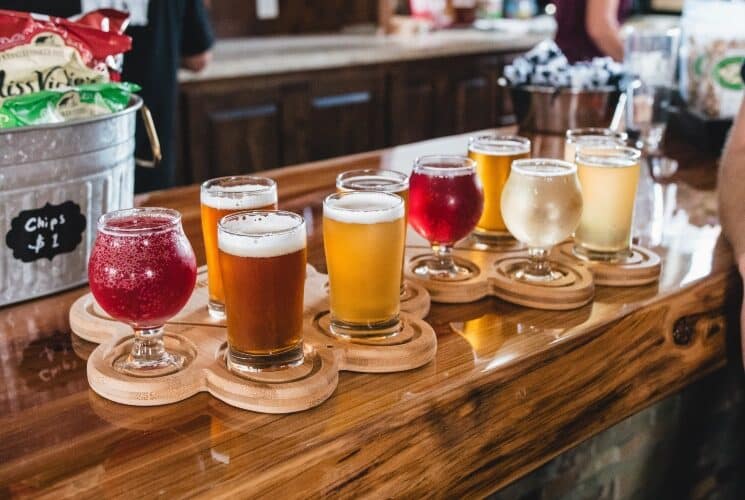 A wood counter at a bar with a flight of 10 different glasses of beer of various colors